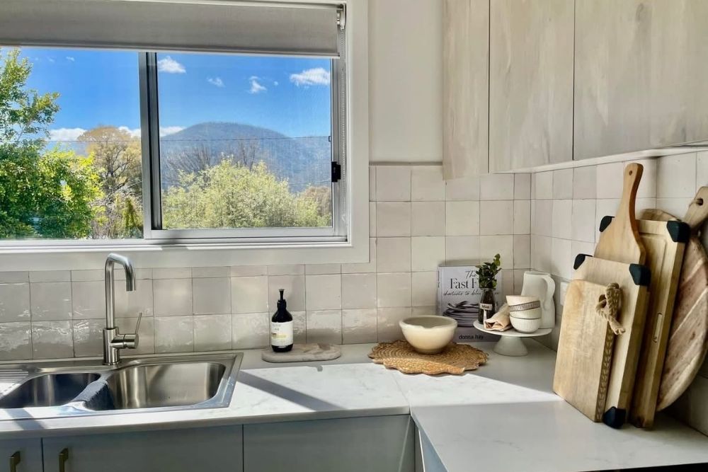 A modern white kitchen featuring stainless steel sink, subway tile backsplash, and views of distant hills-
